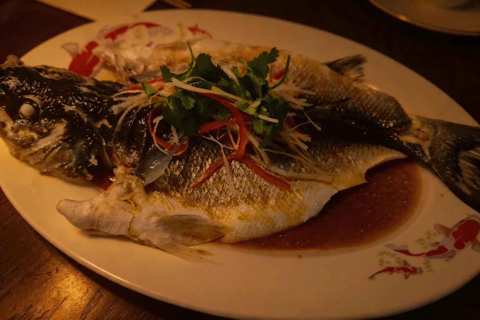 Whole steamed sea bass on a white plate with carp patterns, warm evening light