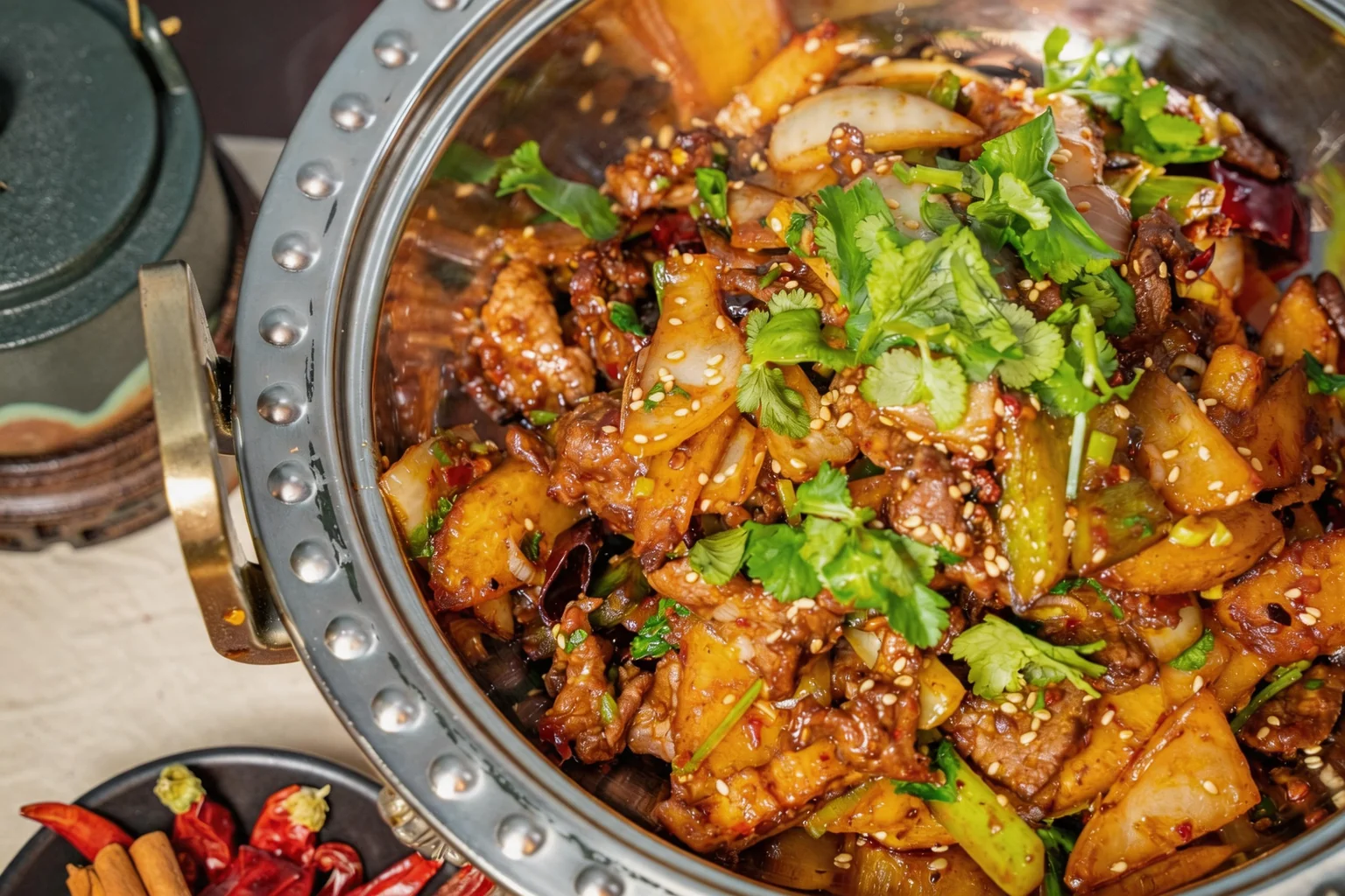 Dish in a metal pot, dried chillies and cinnamon beside it